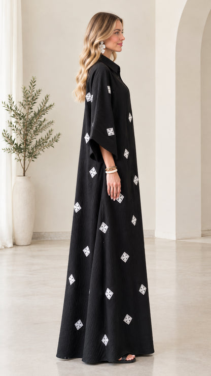 Side profile view of model wearing relaxed black embroidered maxi shirt dress