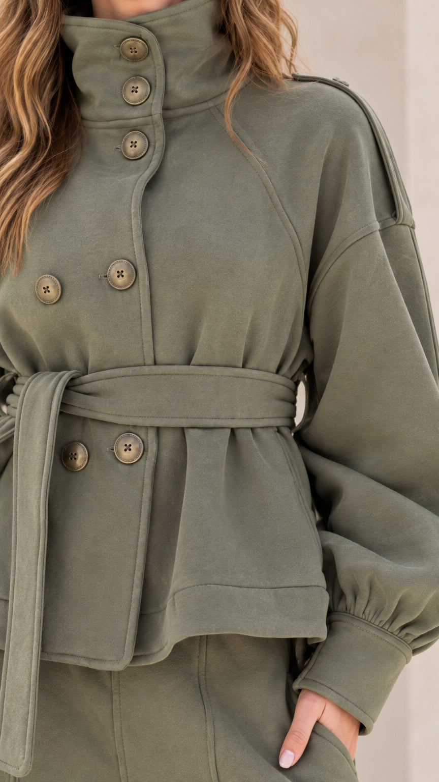 Close-up detail of high stand collar, buttons, and waist tie on olive green jacket