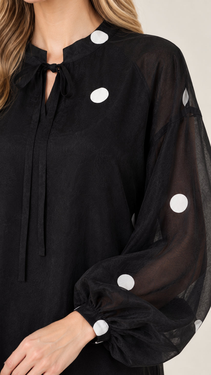 Close-up of tie keyhole neckline and balloon sleeve on black polka dot dress